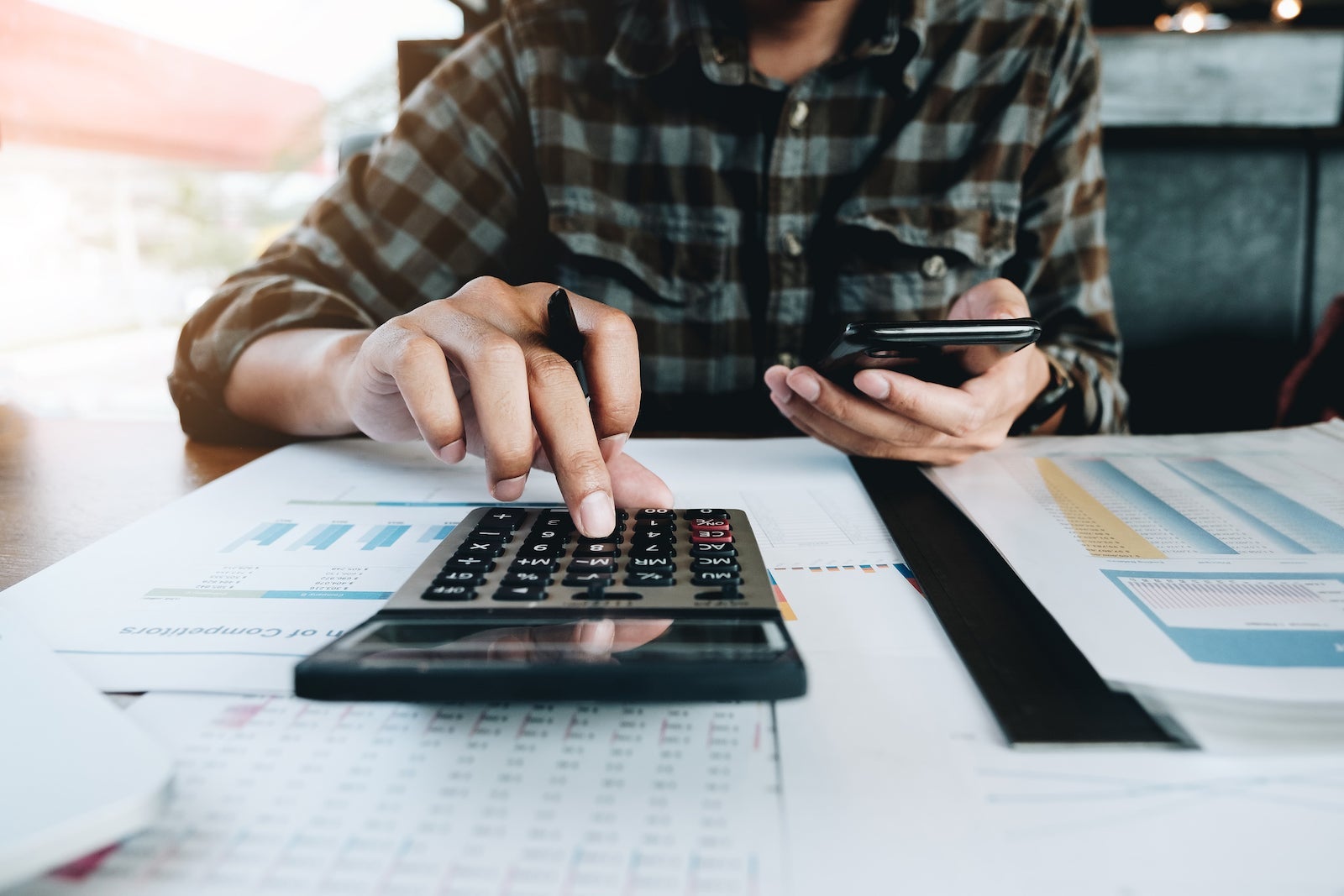 Midsection Of Businessman Using Mobile Phone And Calculator At Desk In Office