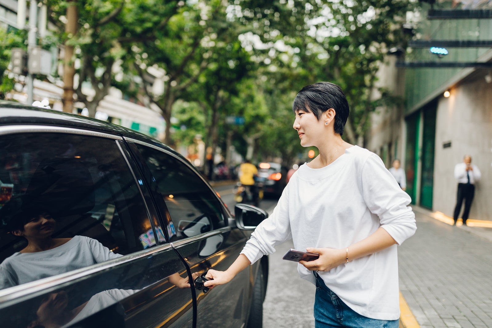 Young Asian woman ordering a taxi ride with mobile app on smartphone in the city.