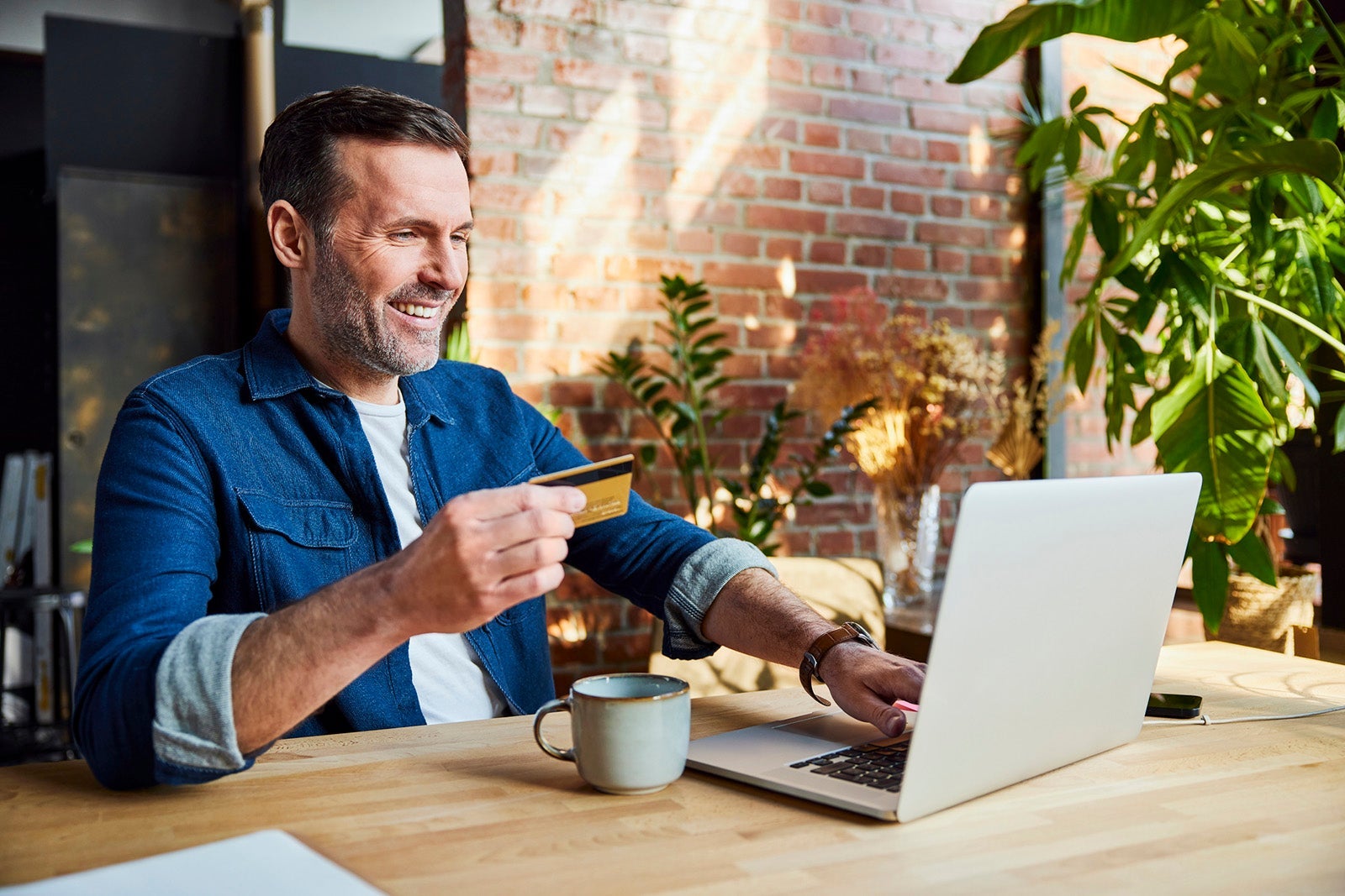 Happy businessman doing online shopping through credit card and laptop at loft office