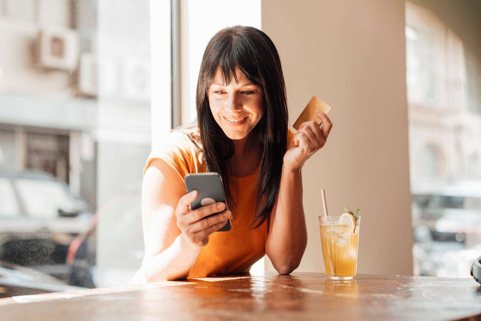 Smiling woman with credit card using smart phone in cafe