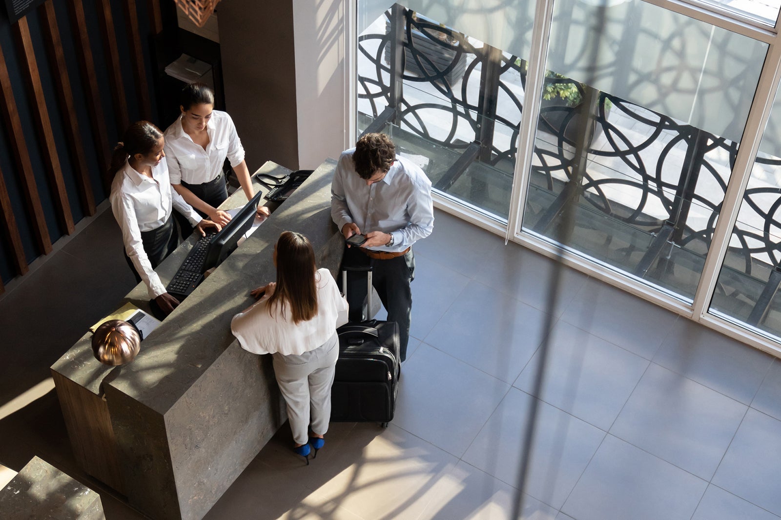 Black manager and recepcionist checking in a couple and man looking at his smartphone