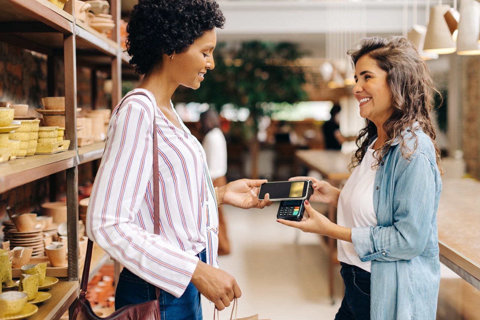 Happy store owner receiving an NFC payment from a customer in her shop