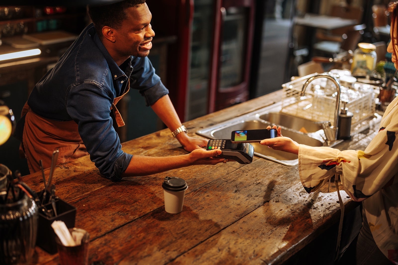 African-American bartender is holding terminal for woman to pay with phone.