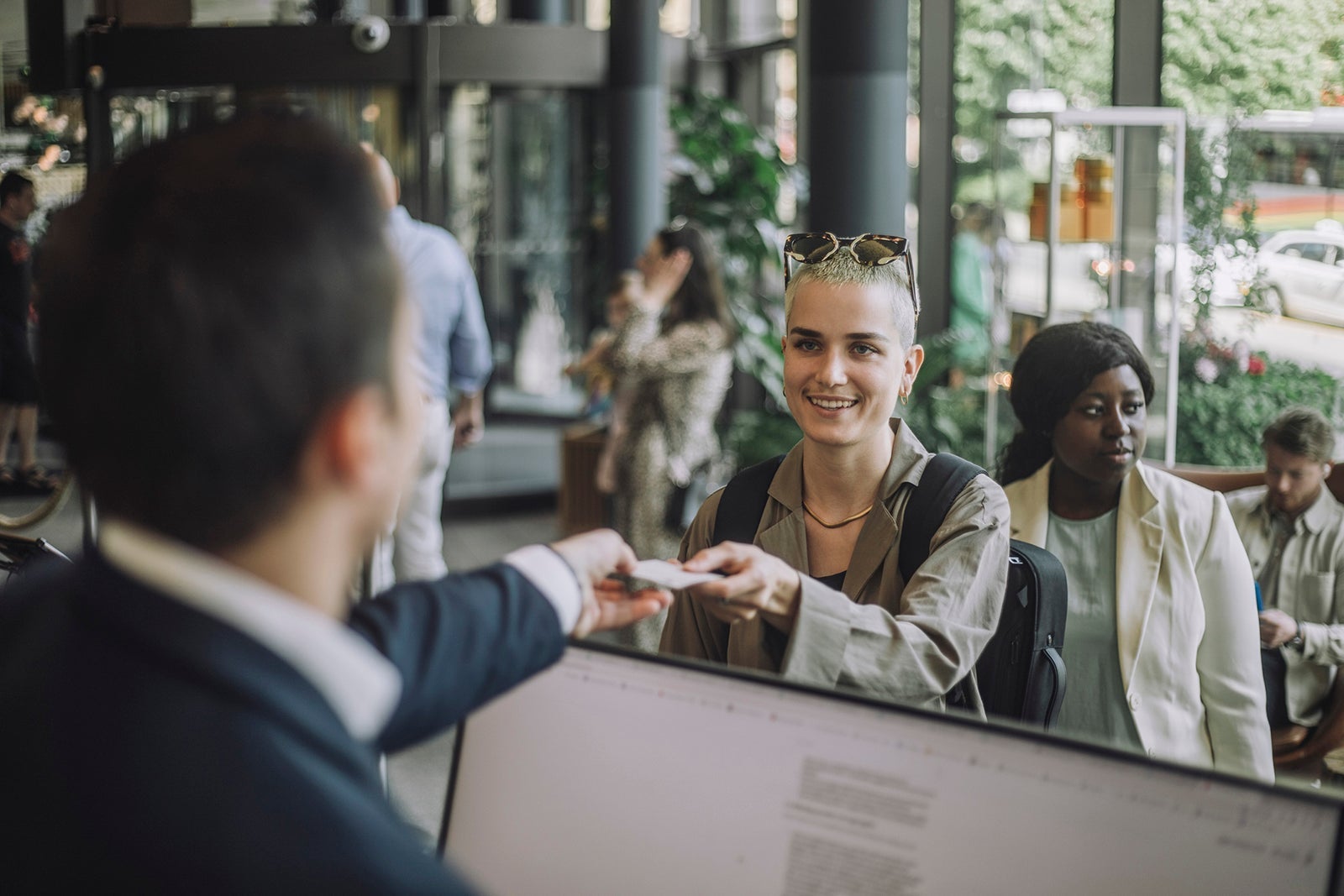 Smiling non-binary person taking keycard from receptionist at hotel