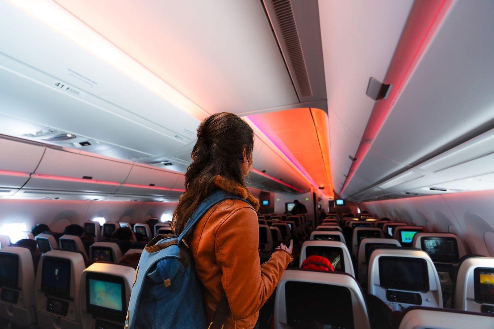 A woman boards a small commercial airplane, carrying a backpack. she walking the aisle on plane