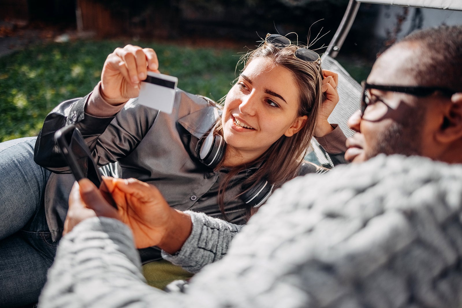 Young adults couple having fun using credit card for on line shopping at home back yard and looking at mobile phone in hand