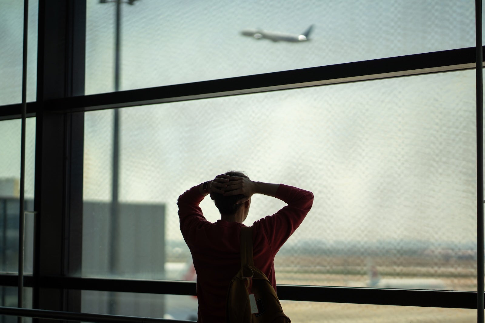 Missed airplane. Stressed man stands before departing airplane through window in airport terminal